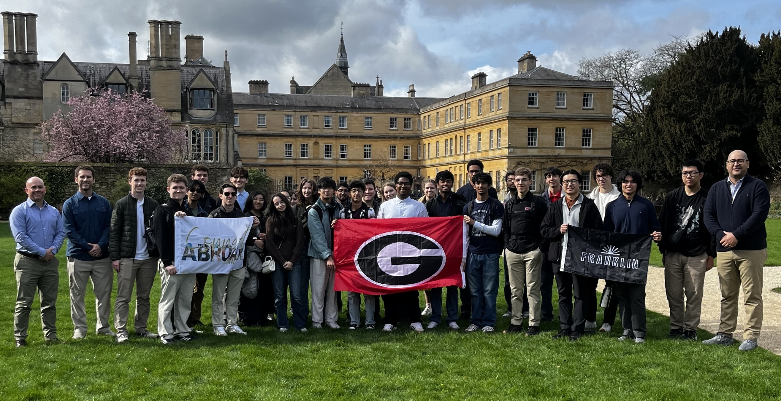 School of Computing faculty, staff, and students posing with a Georgia flag for a photo out on a lawn in London. 